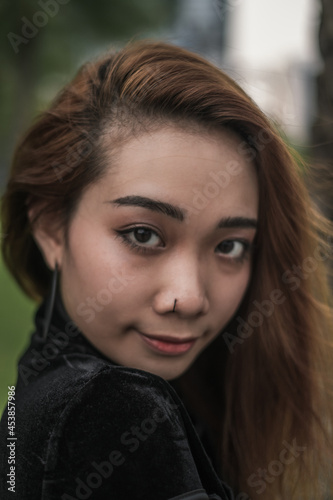 Close-up portrait of beautiful young asian woman outdoor. Wind in her hair. Looking at camera with copy space. Piercing in nose. High quality photo 