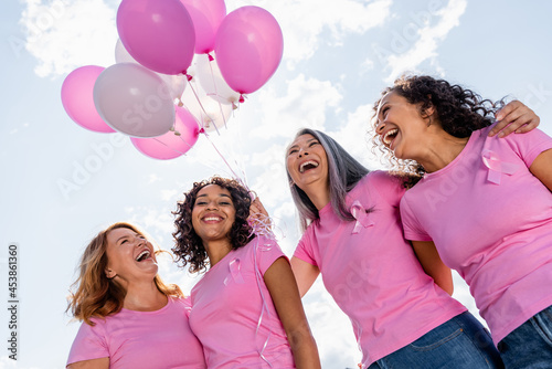 Low angle view of happy multiethnic women with ribbons of breast cancer awareness and balloons outdoors photo