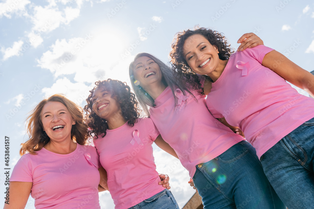 Low angle view of cheerful multicultural women with pink ribbons ...