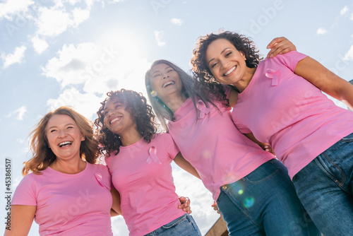 Low angle view of cheerful multicultural women with pink ribbons hugging outdoors photo