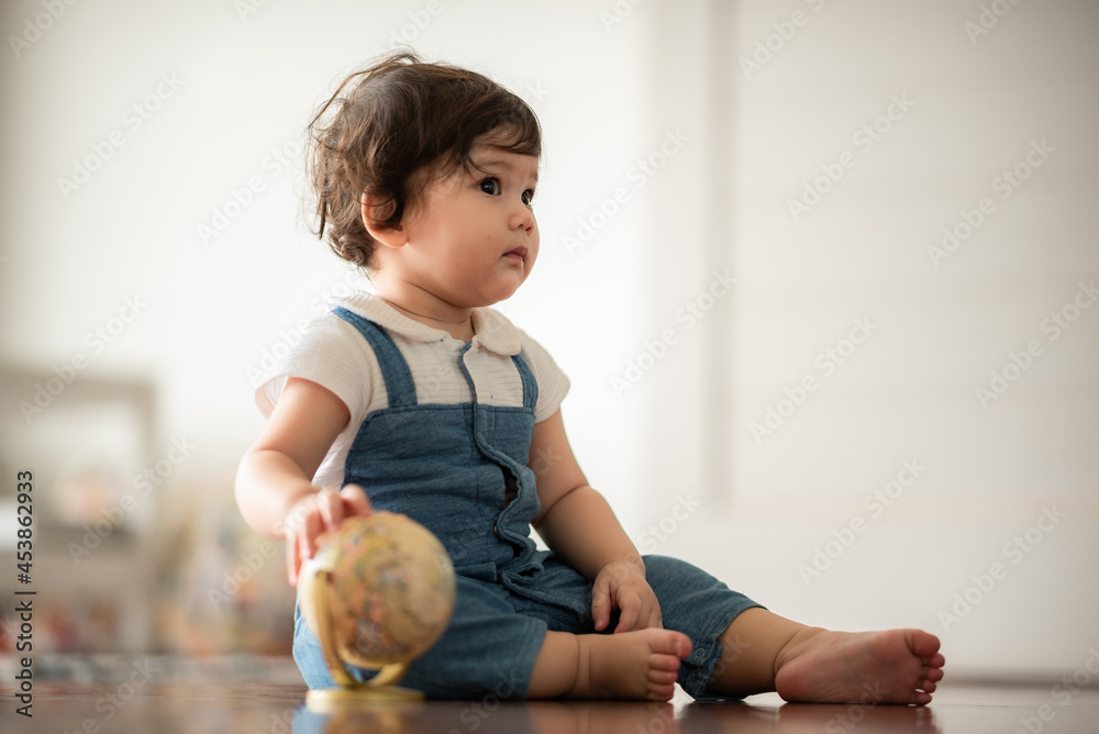 Fototapeta premium Cute little playful girl child learning to walk and stand by taking support of couch at home while looking away mischievously