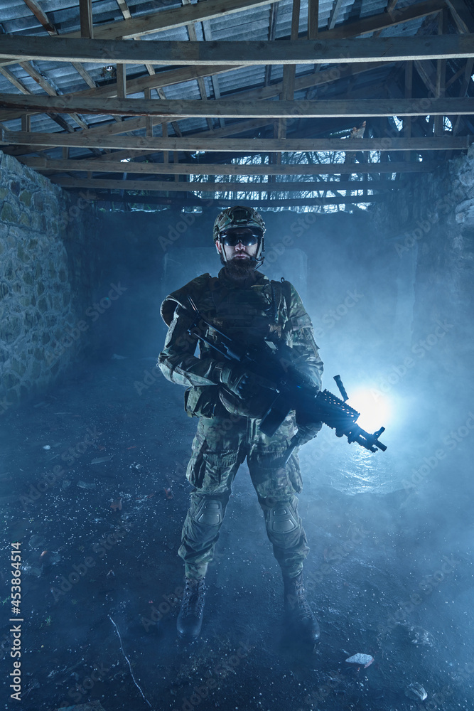 Fototapeta premium Portrait of airsoft player in professional equipment with machine gun in abandoned ruined building. Soldier with weapons at war