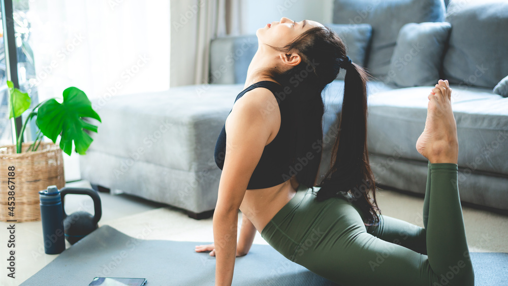 Obraz premium young Asian woman exercise by yoga at home gym, healthy female lifestyle with fitness sport training at home, girl doing body active physical exercise indoor house room, relaxation and wellness