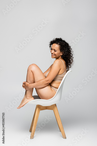 Smiling african american woman in underwear sitting on chair on grey background