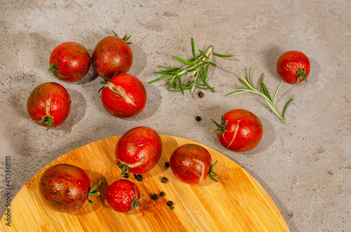 Fresh organic ripe red cherry tomatoes on the kitchen counter and bamboo board. Top view. Branches of rosemary and pepper as a decoration. 