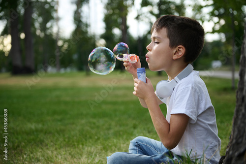 Adorable handsome preadolescent child boy blowing starting soap bubbles on the park, resting during his school recreation