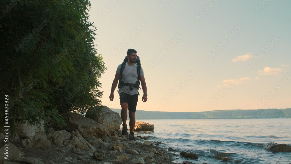 The attractive man with backpack walking along the shore