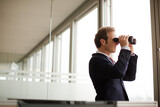 Businessman using binoculars at office window