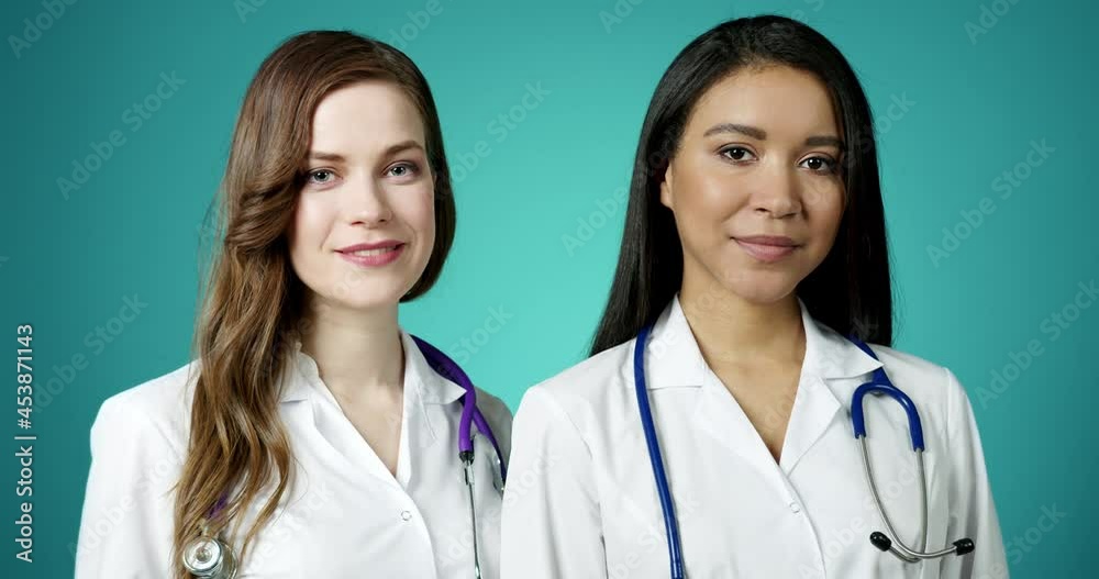 Beautiful Young Happy Medics Girls Smiling at Camera. Two Successful Confident Modern Female Doctors Posing in White Coats Slow Motion. Women Medicine Workers. Health Care and Medicine Concept. Beautiful Young Happy Medics Girls Smiling at Camera. Two Successful Confident Modern Female Doctors Posing in White Coats Slow Motion. Women Medicine Workers. Health Care and Medicine Concept.