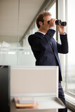 Businessman using binoculars at office window