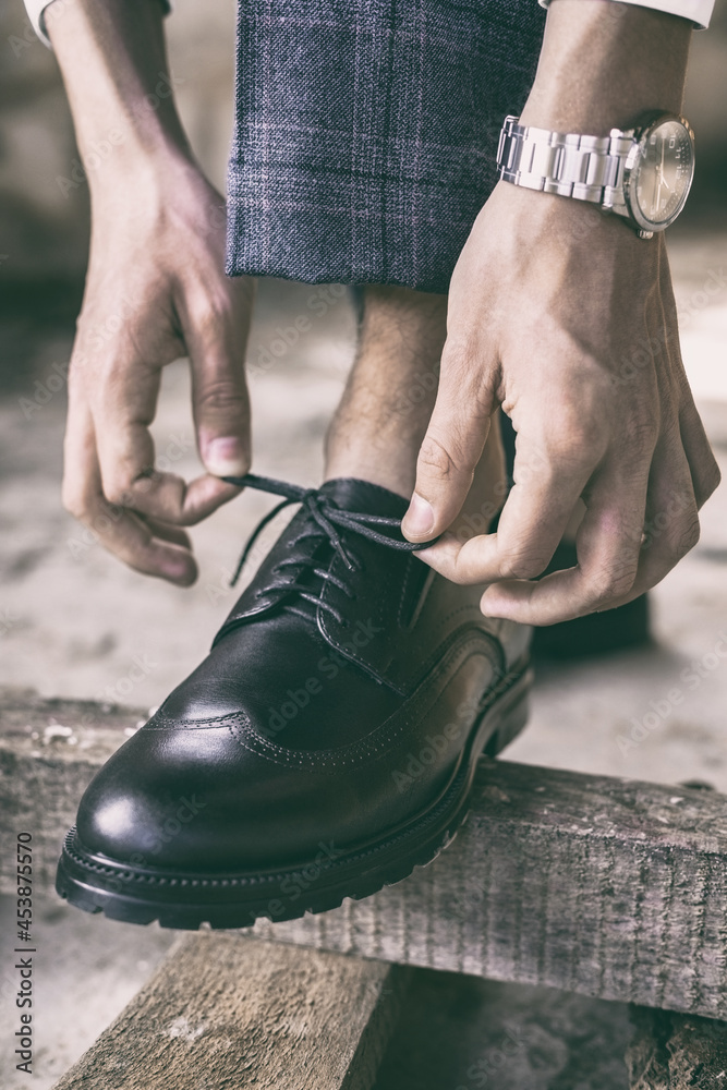 close-up young man ties his shoelaces on stylish black shoes