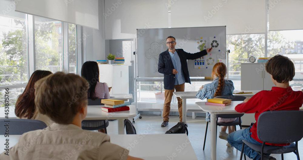 Back view of multiethnic teen students in classroom listen to teacher and raise hand to answer question Back view of multiethnic teen students in classroom listen to teacher and raise hand to answer question