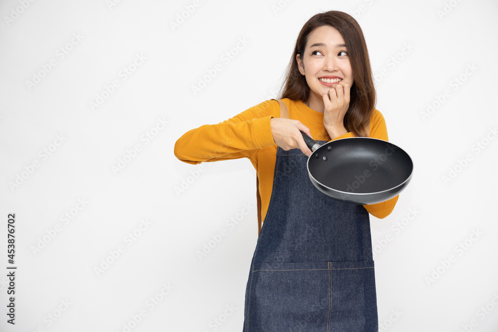 Happy young Asian female housewife wearing kitchen apron cooking and holding pan isolated on white background Happy young Asian female housewife wearing kitchen apron cooking and holding pan isolated on white background