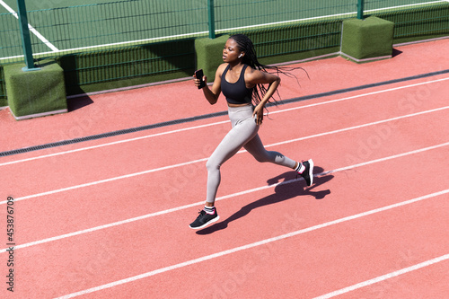 Confident african female athlete running on racetrack. Sportive black sport woman training jog on stadium prepare for competition event, marathon or triathlon. Mix race girl runner practicing outdoor