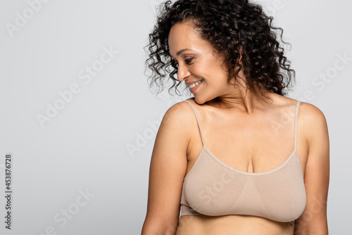 Side view of smiling african american woman in bra isolated on grey, body positive concept