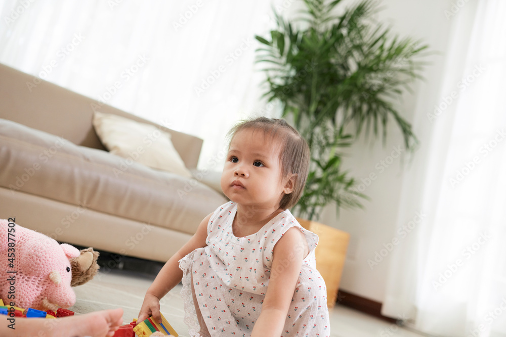 Cute serious toddler girl playing with colorful plastic brick blocks on the floor in living room Cute serious toddler girl playing with colorful plastic brick blocks on the floor in living room