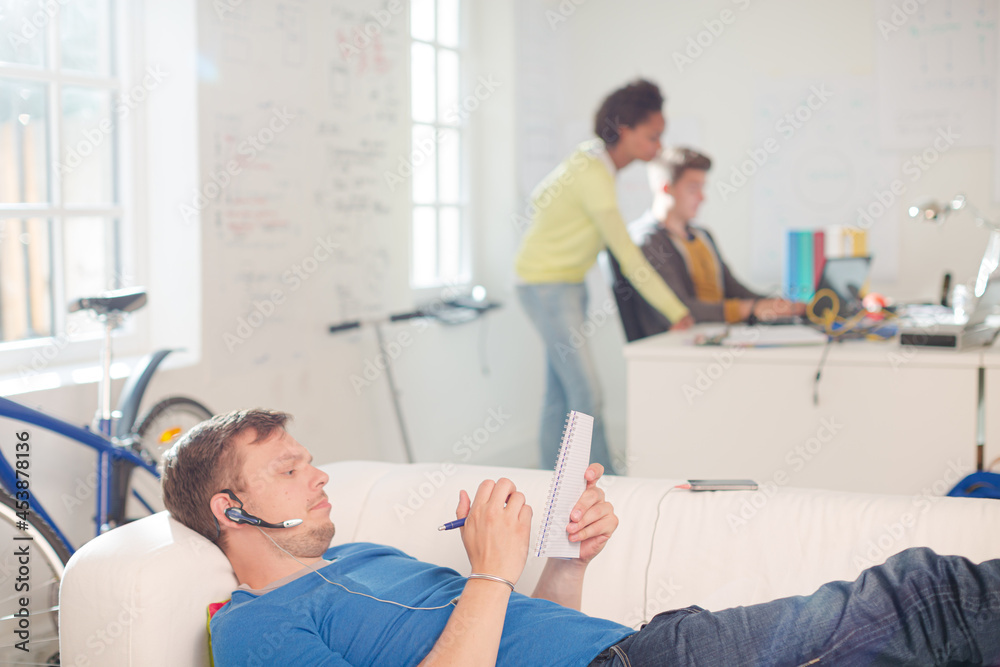 Obraz premium Man in headset taking notes on sofa