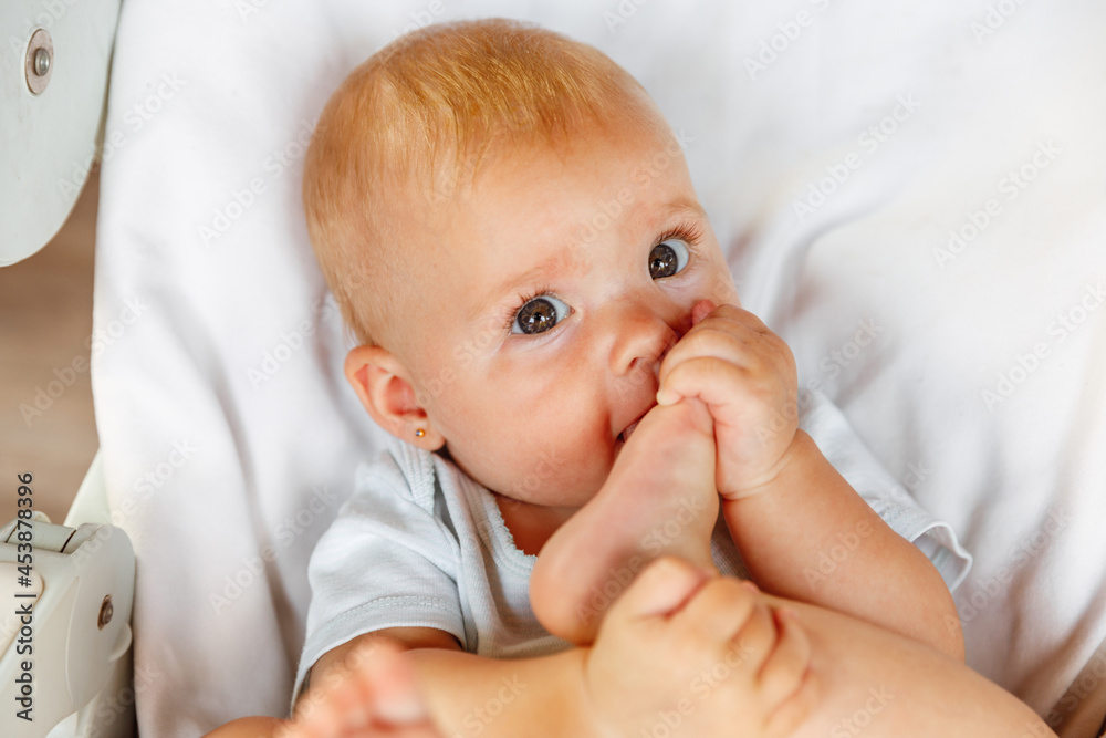 Cute little newborn girl with funny face sucking foot toe on white background. Infant baby resting playing lying down on feeding chair at home. Motherhood happy child concept Cute little newborn girl with funny face sucking foot toe on white background. Infant baby resting playing lying down on feeding chair at home. Motherhood happy child concept