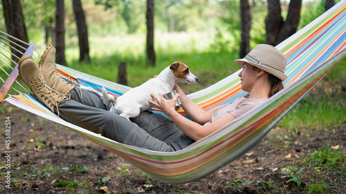 Caucasian woman lies in a hammock with Jack Russell Terrier dog in a pine forest © Михаил Решетников