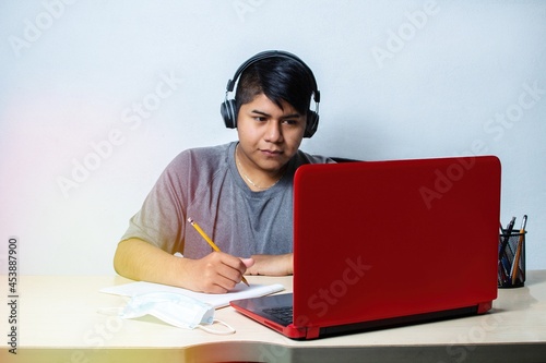 young latin man with headphones typing in front of laptop. mexican teenager