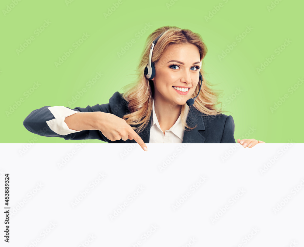 Call center. Customer support service female phone operator or sales agent in headset, grey confident suit pointing at mock up signboard with copy space for text, isolated over light green background. Call center. Customer support service female phone operator or sales agent in headset, grey confident suit pointing at mock up signboard with copy space for text, isolated over light green background.