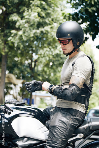 Motorcyclist taking on leather gloves, helmet and guard pads for protection