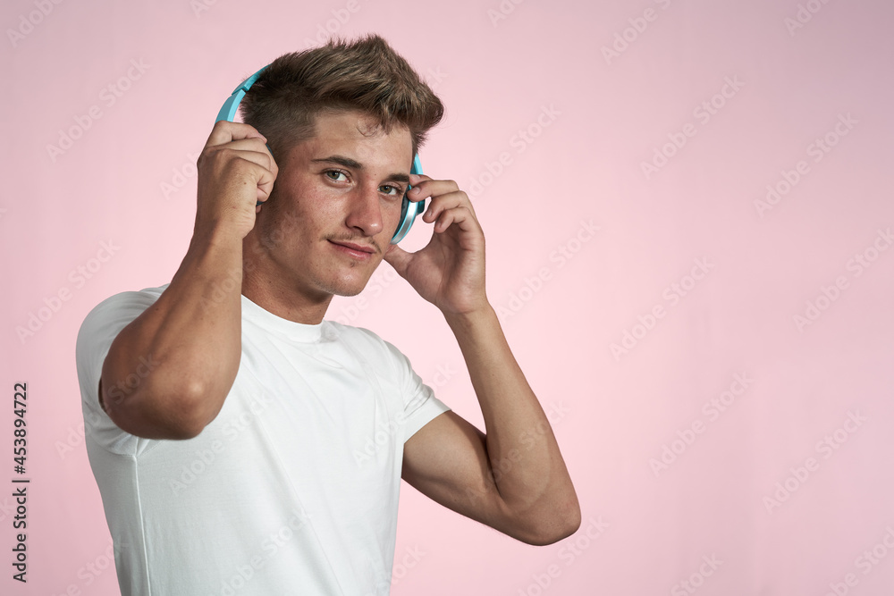 Young man in white t-shirt putting on headphones. Pastel pink background Young man in white t-shirt putting on headphones. Pastel pink background