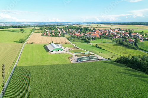 Aerial shot of a cow farmer business with a beautiful vilylage next to it, surrounded by nature.
