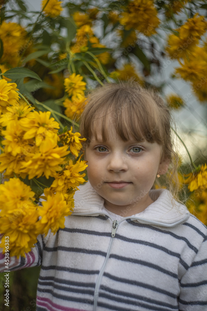 a small blonde girl stands against a background of yellow flowers a small blonde girl stands against a background of yellow flowers