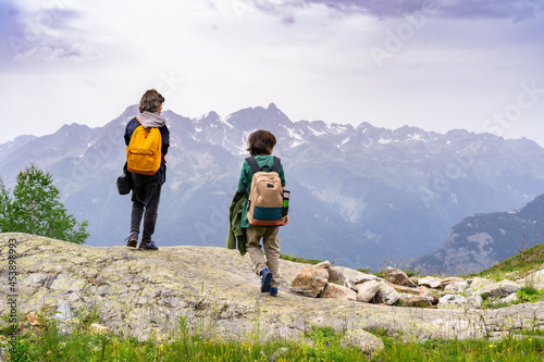 Two boys with backpacks behind them standing on the top of the mountain, resting after a long ascent. Active vacation concept. Hiking in family.