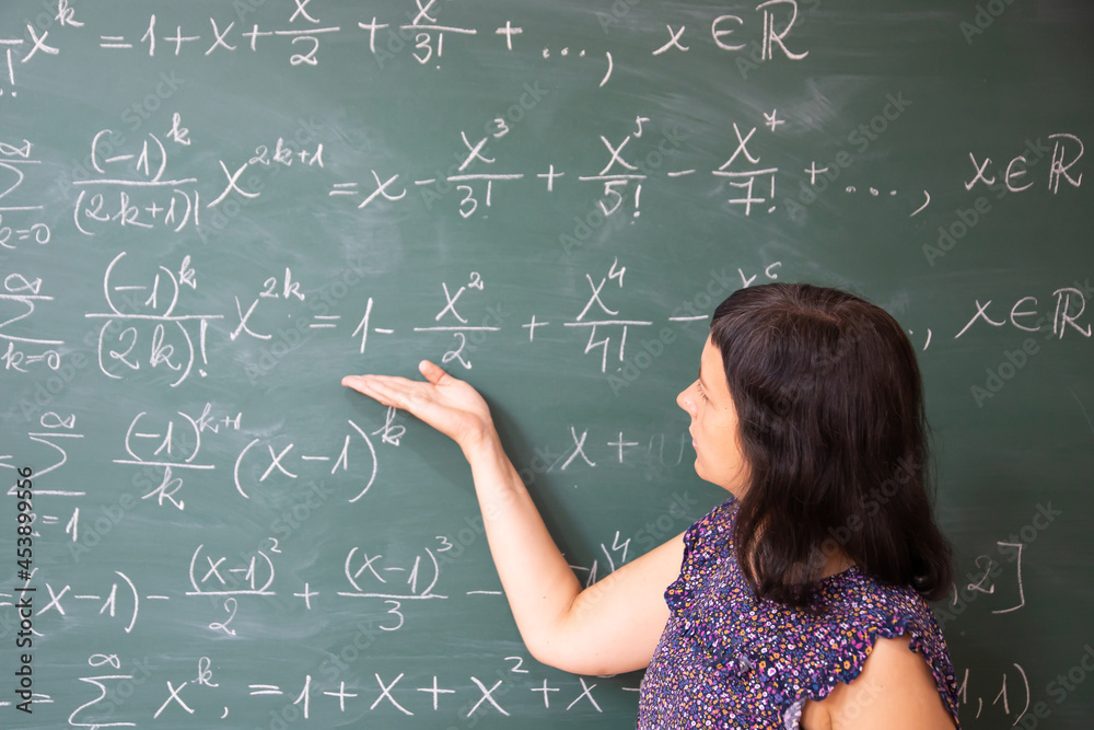 Female student or teacher in the classroom writing on chalkboard mathematical equations Female student or teacher in the classroom writing on chalkboard mathematical equations