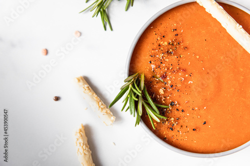 Tomato soup garnish with ground pepper, rosemary and bread sticks, light background.