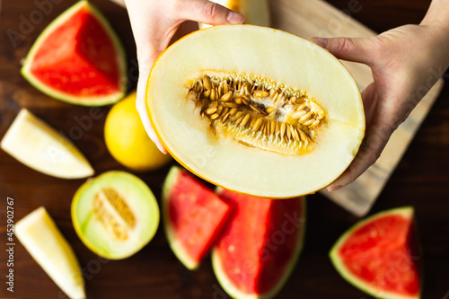 Two hands holding honeydew melon with different melons in the background; half a ripe honeydew melon with seeds