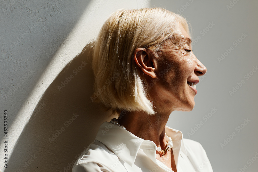Minimal side view portrait of elegant mature woman lit by sunlight against  white wall, copy space Stock Photo | Adobe Stock