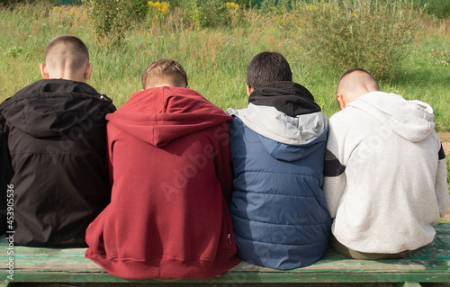 Four teenagers are sitting on a wooden bench with their backs turned away.