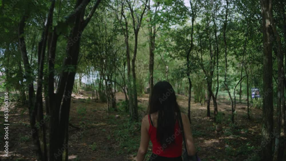 Rearview of Asian woman walking in the middle of nature with a mat and water bottle for practicing yoga. yoga practice and healthy lifestyle concept Rearview of Asian woman walking in the middle of nature with a mat and water bottle for practicing yoga. yoga practice and healthy lifestyle concept