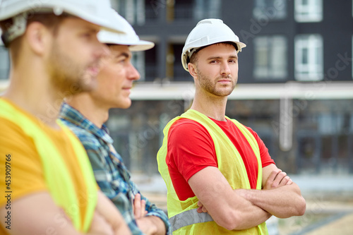 Serious builder in a safety vest accompanied by his colleagues photo