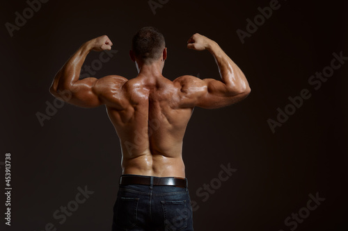 Male muscular athlete poses in studio, back view