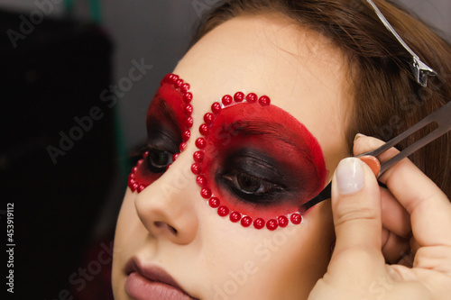 Makeup artist gluing sequins on the rim of a young girl's eyes.