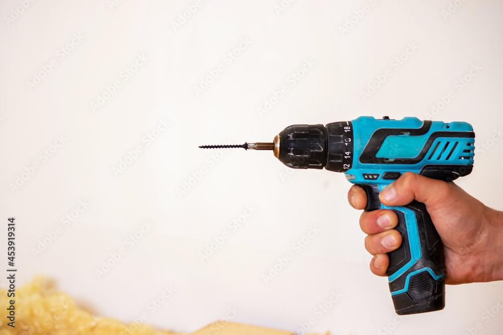 Hand with cordless screwdriver and drill isolated on white background. Twists screws into the board.