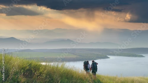 The two tourists standing on mountain top on beautiful river background
