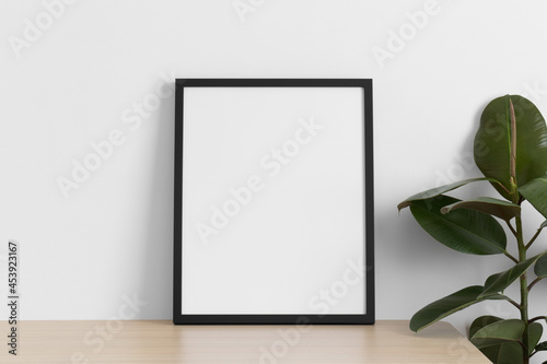 Black frame mockup on the wooden table with a ficus plant.