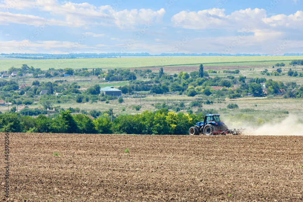 Fototapeta premium Tractor in the field cultivates the soil after the harvest.