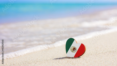 Flag of Mexico in the shape of a heart on a sandy beach. The concept of the best vacation in Mexican resorts.