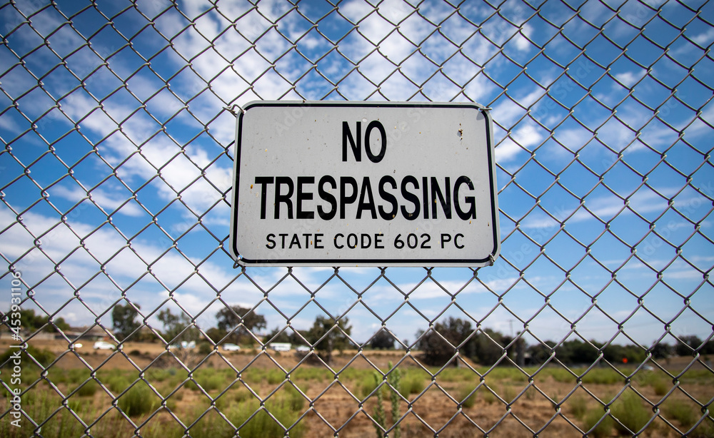 A sign stating No Trespassing on a chain link fence against a blue sky with negative space A sign stating No Trespassing on a chain link fence against a blue sky with negative space