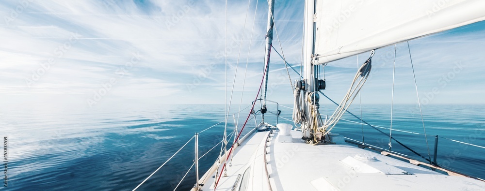 White sloop rigged yacht sailing in an open Baltic sea on a clear sunny day. A view from the deck to the bow, mast and sails. Estonia - obrazy, fototapety, plakaty 