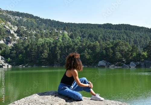 Black woman with curly afro hair sitting on top of a rock. Observing the Black Lagoon and the pine forest in Soria, Spain. photo