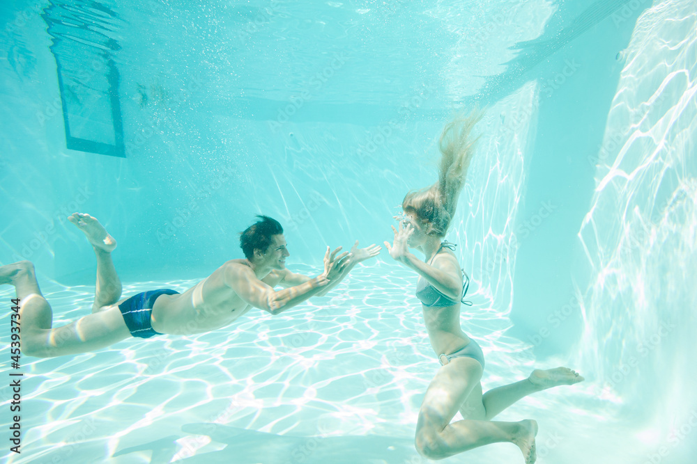Couple swimming underwater in pool