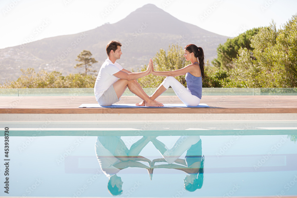 Couple practicing yoga at poolside