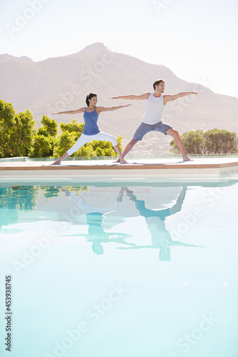 Man and woman practicing yoga at poolside